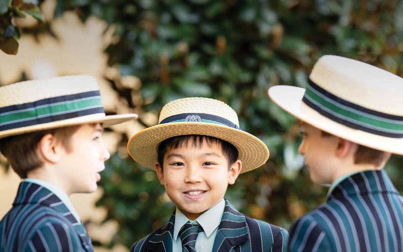 Three Year 5 students are standing talking. One of the students is looking directly at the viewer and smiling. All are wearing full BBC uniforms with their boater hats on.