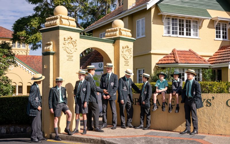 Students from every year level standing and sitting at the front gates of Brisbane Boys' College on Kensington Terrace.